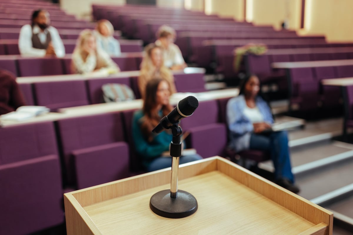 Microphone on podium with university students sitting in an amphitheater listening to a lecture