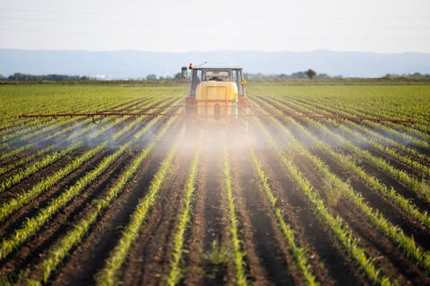 Tractor spraying pesticides in sunset field