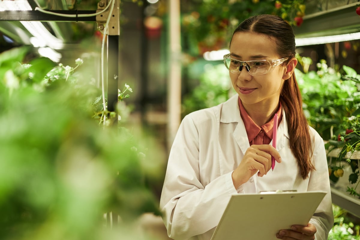 Young woman working in greenhouse monitoring growth