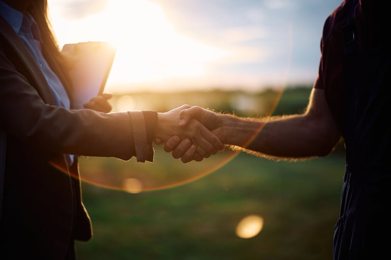 Close up of businesswoman and farm owner shaking hands in the field at sunset.