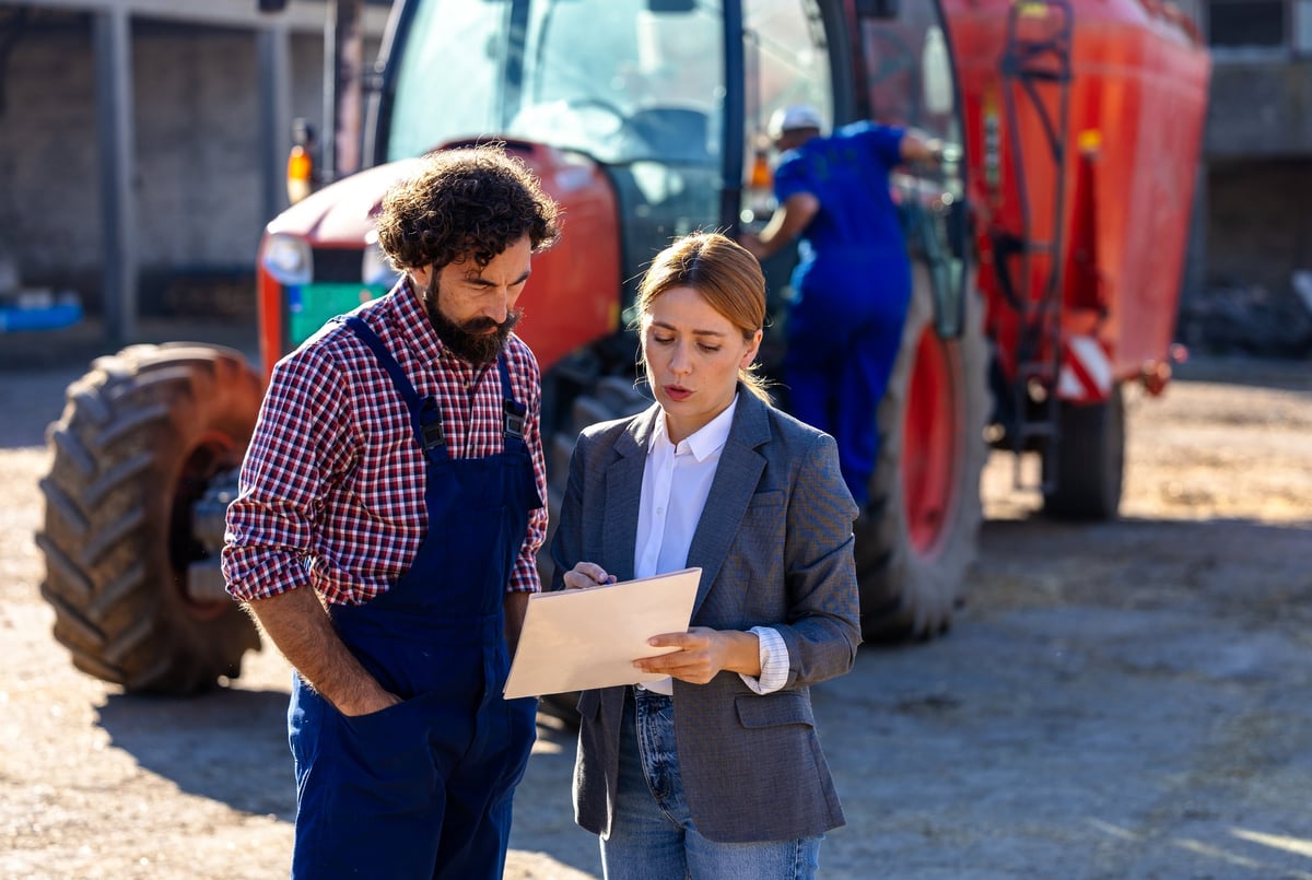 Farmer and business woman discuss farm operations while standing near a tractor