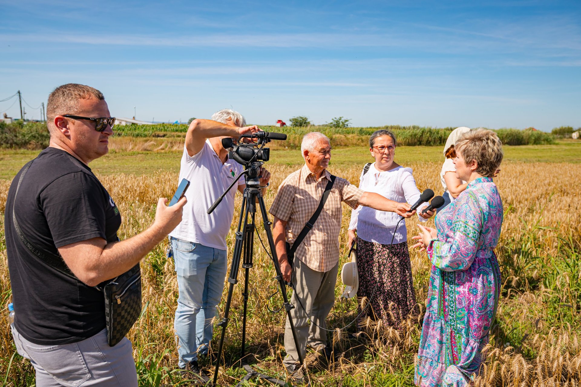 Videographer and journalist conducting field interview in wheat field
