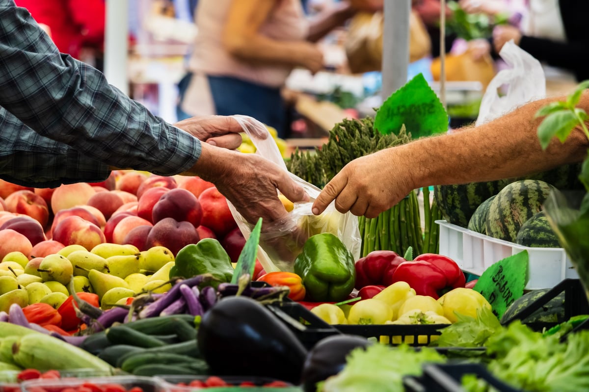 Buyers and vendors exchange fresh vegetables at a busy farmers market