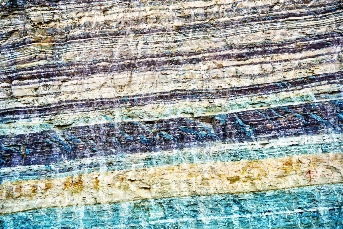 Sedimentary rock layers in an anti atlas road cut, colorful horizontal strata of blue, white, brown and purple creating an abstract, textured geological pattern and cross section