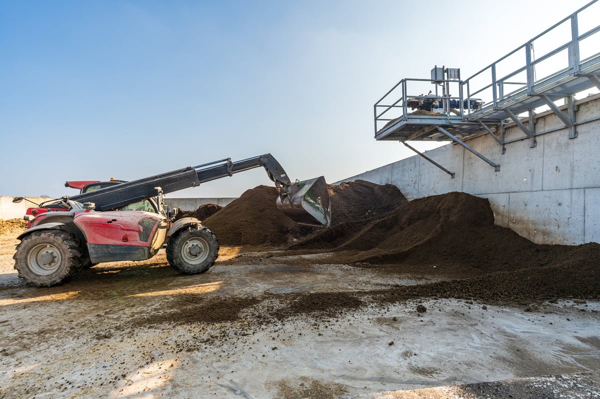 A red telehandler moves a pile of solid digestate in a modern biogas facility, showing industrial waste processing and sustainability.