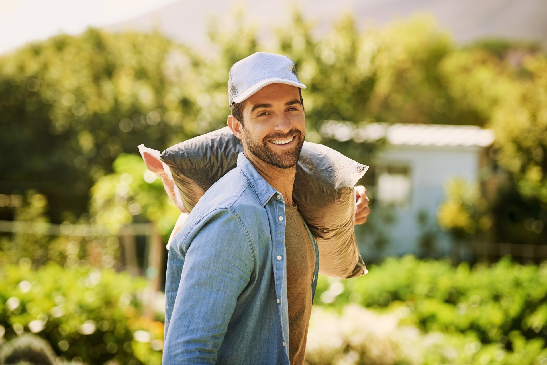 Portrait of a happy young farmer carrying a bag of compost over his shoulder on the farm