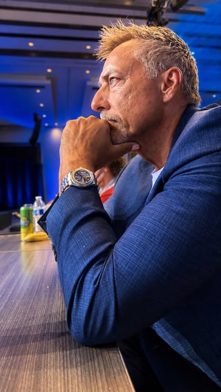 Middle-aged man in blue suit with hand to chin, contemplating in modern conference room with blue lighting