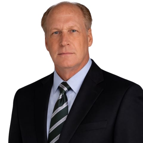 Professional headshot of a middle-aged man with light brown hair wearing a black blazer, light blue dress shirt, and striped tie against a white background