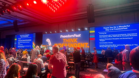 Large indoor event venue with crowd viewing FreedomFest stage display featuring neon signage and red and blue lighting