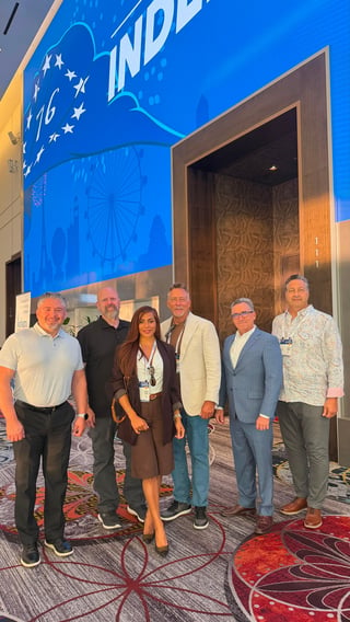 Six professionals posing together in front of a blue Indianapolis convention center backdrop with modern elevator doors