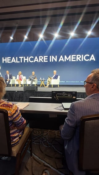 Panel discussion on Healthcare in America at conference, with four speakers seated on stage and audience members viewing from seats below