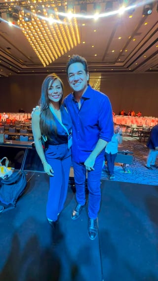 Two people smiling at camera in formal blue attire at an upscale event venue with elegant lighting and table settings