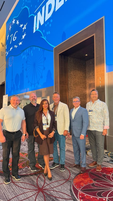 Six professionals posed together at an indoor event with blue signage and decorative flooring in background